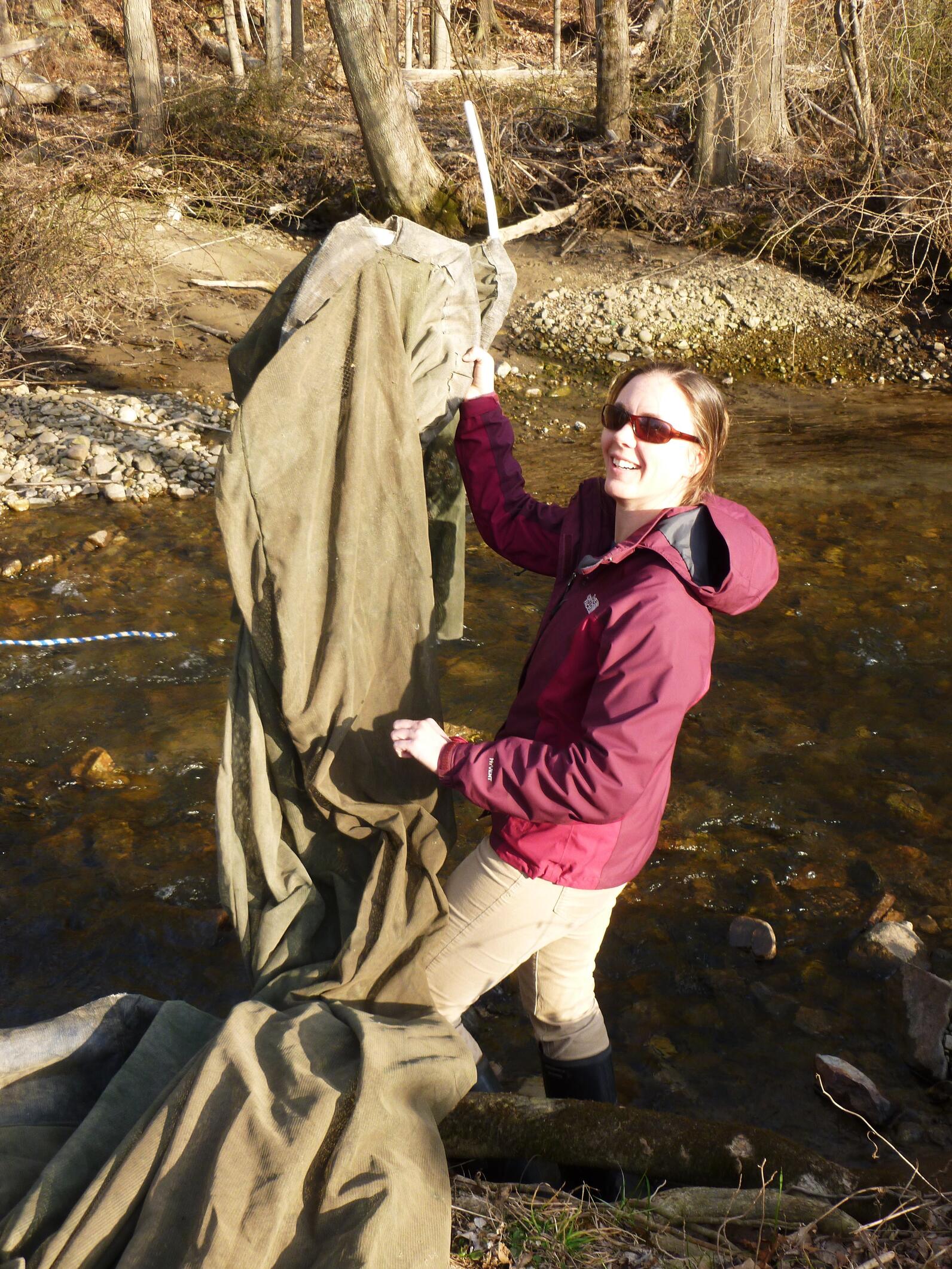 Rebecca Schultz standing in water outside while holding a large net and smiling.